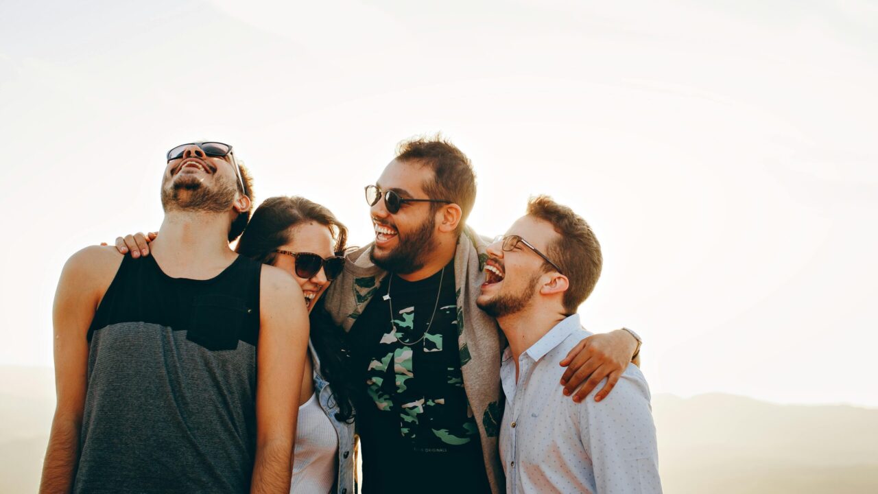 A group of young adults laughing and enjoying time together outdoors under the sun.
